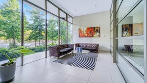 Um quarto amplo, com grandes janelas, sofá modular, mesa de centro e arte abstrata na parede.