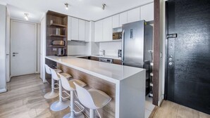 Cozinha moderna com armários brancos, geladeira de aço inoxidável e um balcão com banquetas brancas.
