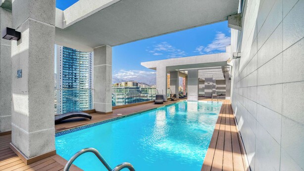 Piscina no terraço com água azul cristalina, deck de madeira e vista para edifícios altos.