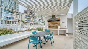 An outdoor patio with a grill, seating, and a view of high-rise buildings. - Infinite Coast 2BR with pool, gym & free parking (Viña del Mar)