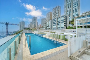 A rooftop swimming pool with a cityscape view, surrounded by modern high-rise buildings.
