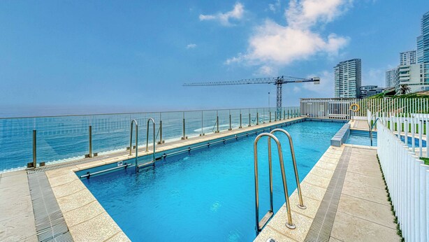 A swimming pool with a view of the ocean and a construction crane in the background. - Infinite Coast 2BR with pool, gym & free parking (Viña del Mar)