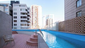 A swimming pool area with steps leading into the water, surrounded by modern buildings. - La Gloria Home - Comfort and City Views (Las Condes)