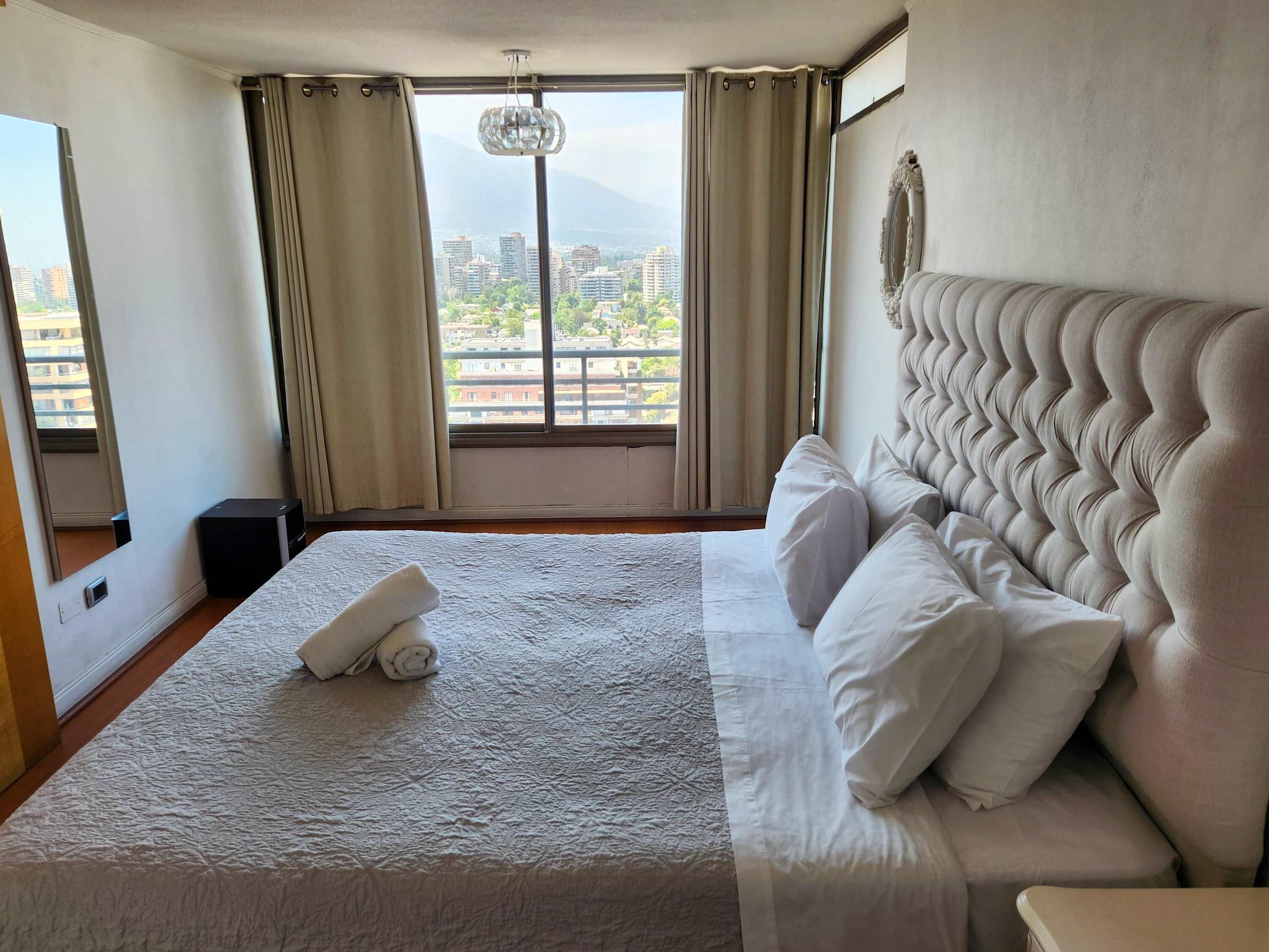 A hotel room with a large bed, a view of the city, and a chandelier.