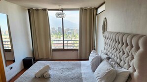 A hotel room with a large bed, a view of the city, and a chandelier. - La Gloria Home - Comfort and City Views (Las Condes)