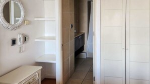 A bathroom with a toilet, sink, and mirror. There is a white cabinet with drawers and a small shelf. - La Gloria Home - Comfort and City Views (Las Condes)