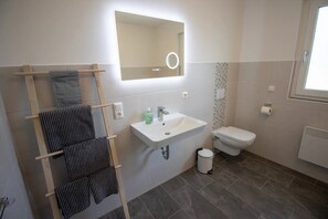Une salle de bain avec un lavabo blanc, des toilettes, un porte-serviettes avec des serviettes à rayures, un miroir avec un éclairage et une fenêtre.