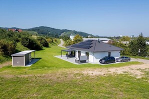 A modern house with solar panels, a covered patio, and a car parked in the driveway.
