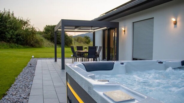 A hot tub with a pergola, a patio with chairs, and a view of the outdoors.