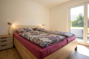 A bedroom with a bed, bedside tables, and a view of greenery outside.