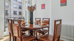 Un comedor con una mesa redonda, seis sillas y un florero con flores secas.