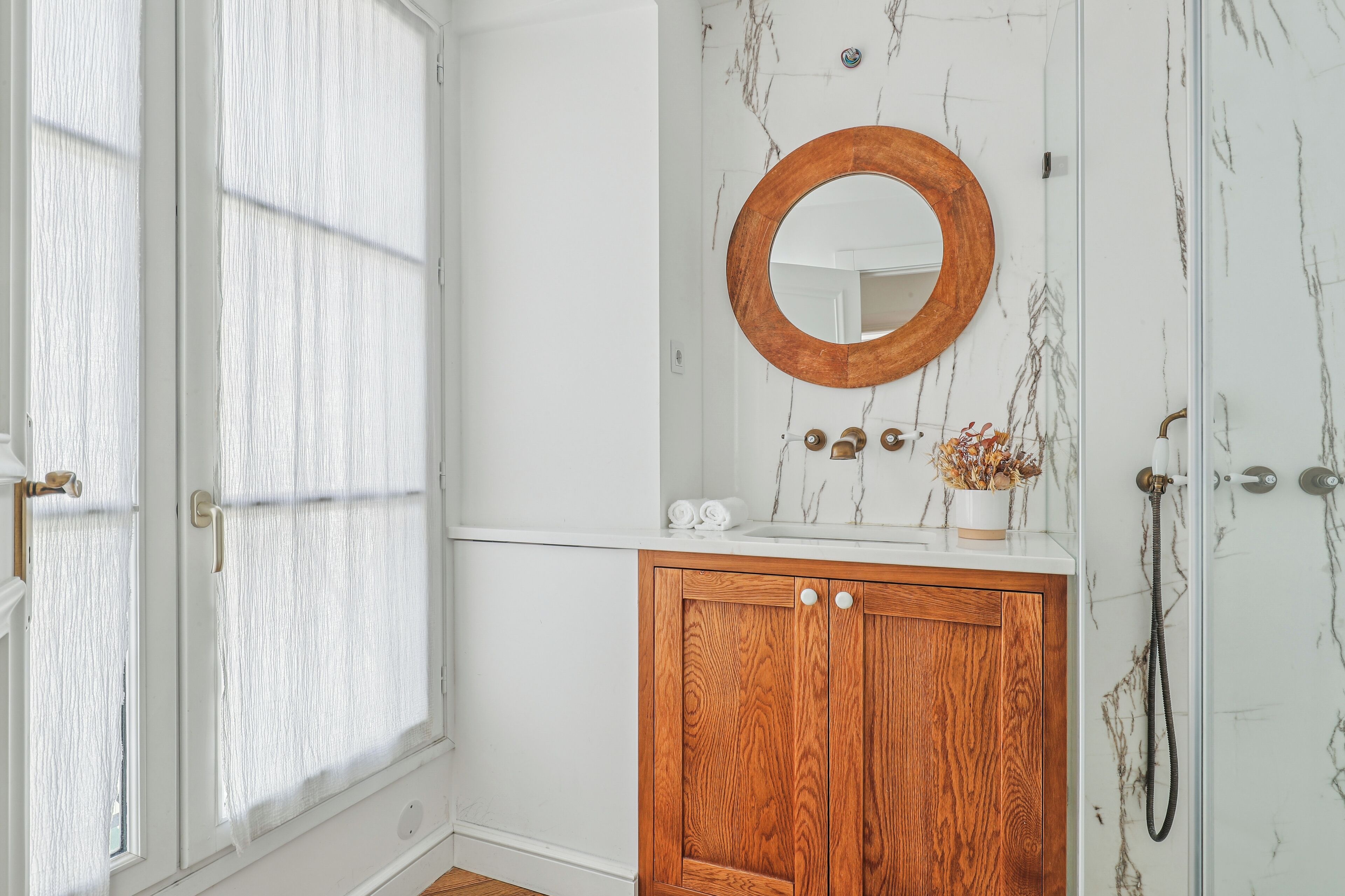 Un baño con tocador de madera, pared de mármol, espejo con marco de madera y ducha.