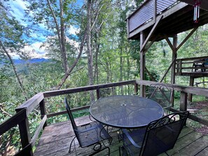 A wooden deck with a round table and chairs, surrounded by a wooden railing, overlooking a forested area. - Cozy Condo for Adventurous Couples in Sugar Mountain (Sugar Mountain)
