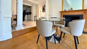 Een eetgedeelte met een ronde glazen tafel en vier stoelen, een open haard en een grote spiegel aan de muur.