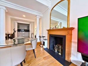 Un salon moderne avec une table à manger en verre, des chaises blanches, une cheminée et un grand miroir.