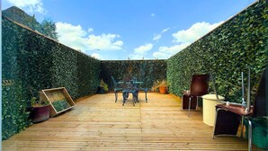 Een houten terras met een tafel en stoelen, omgeven door een hoge haag.