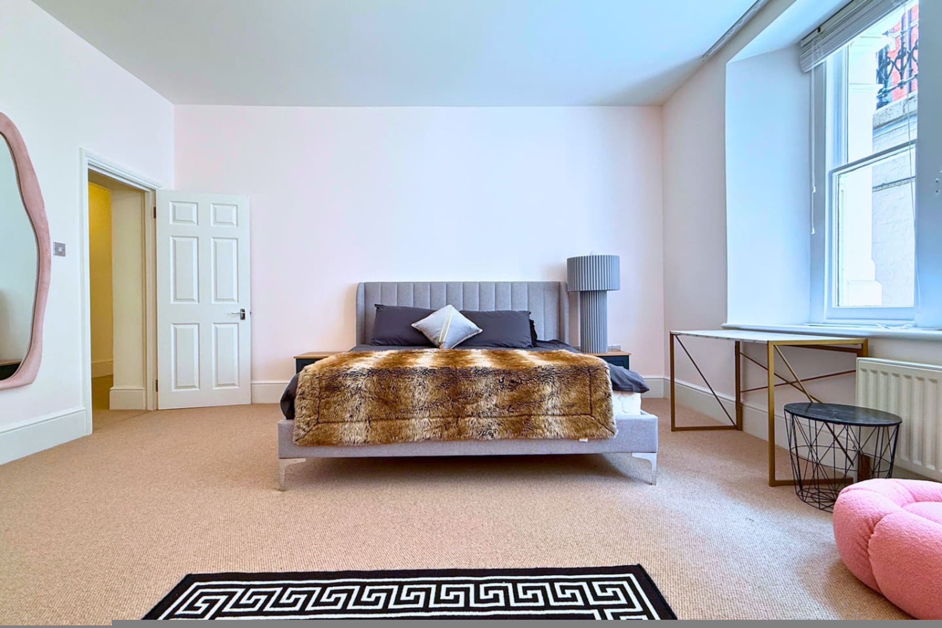 A bedroom with a bed, a bedside table, a lamp, a window, and a door.