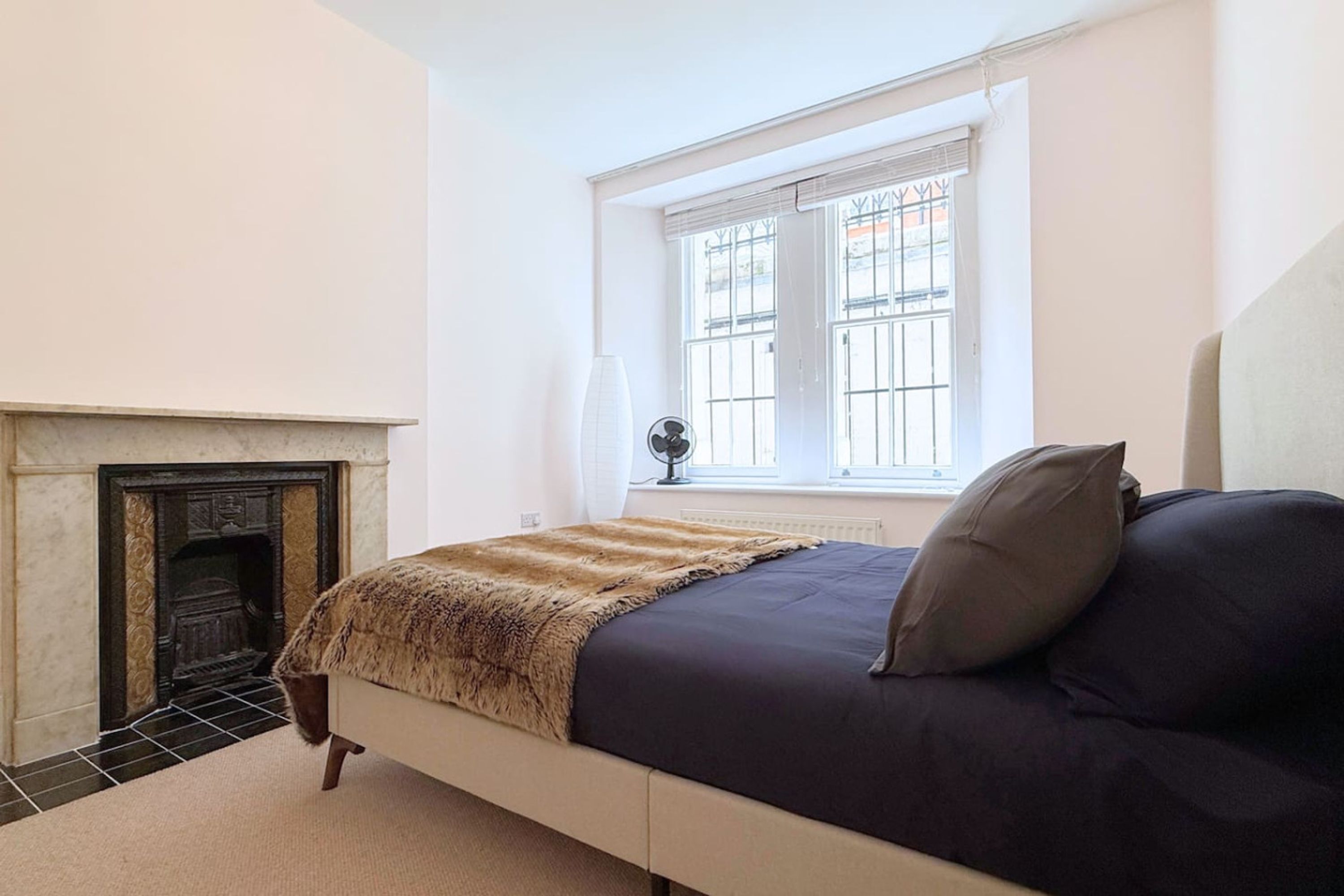 A bedroom with a bed, a fireplace, a window with bars, and a radiator.