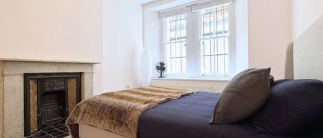 A bedroom with a bed, a fireplace, a window with bars, and a radiator.