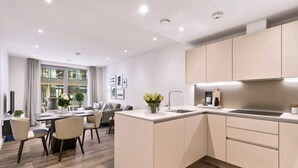 A modern kitchen with a central island, a dining area with a table and chairs, and a large window providing natural light. - 2bed-2bath-2balconylondoneyeview (London)