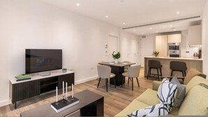 A modern living room with a flat-screen TV, a coffee table with candles, and a sofa. The room connects to a kitchen with a dining area. - 2bed-2bath-2balconylondoneyeview (London)