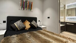 Ein modernes Schlafzimmer mit einem schwarzen Kopfteil, einem Fellüberwurf und einem farbenfrohen, abstrakten Gemälde an der Wand.