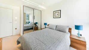 A modern bedroom with a large bed, a wardrobe, and a mirror. - Aldgate (London)