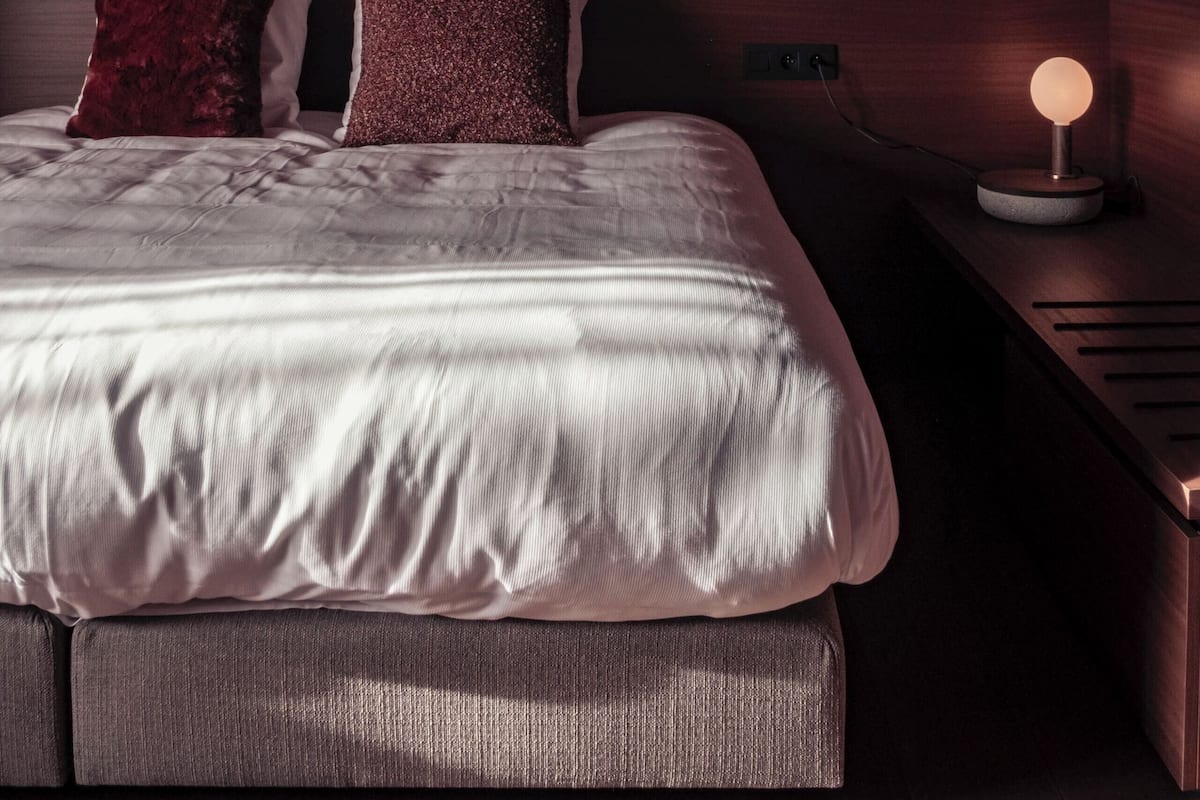 Un dormitorio moderno con una cama grande, dos almohadas, una mesita de noche con una lámpara y un techo inclinado.