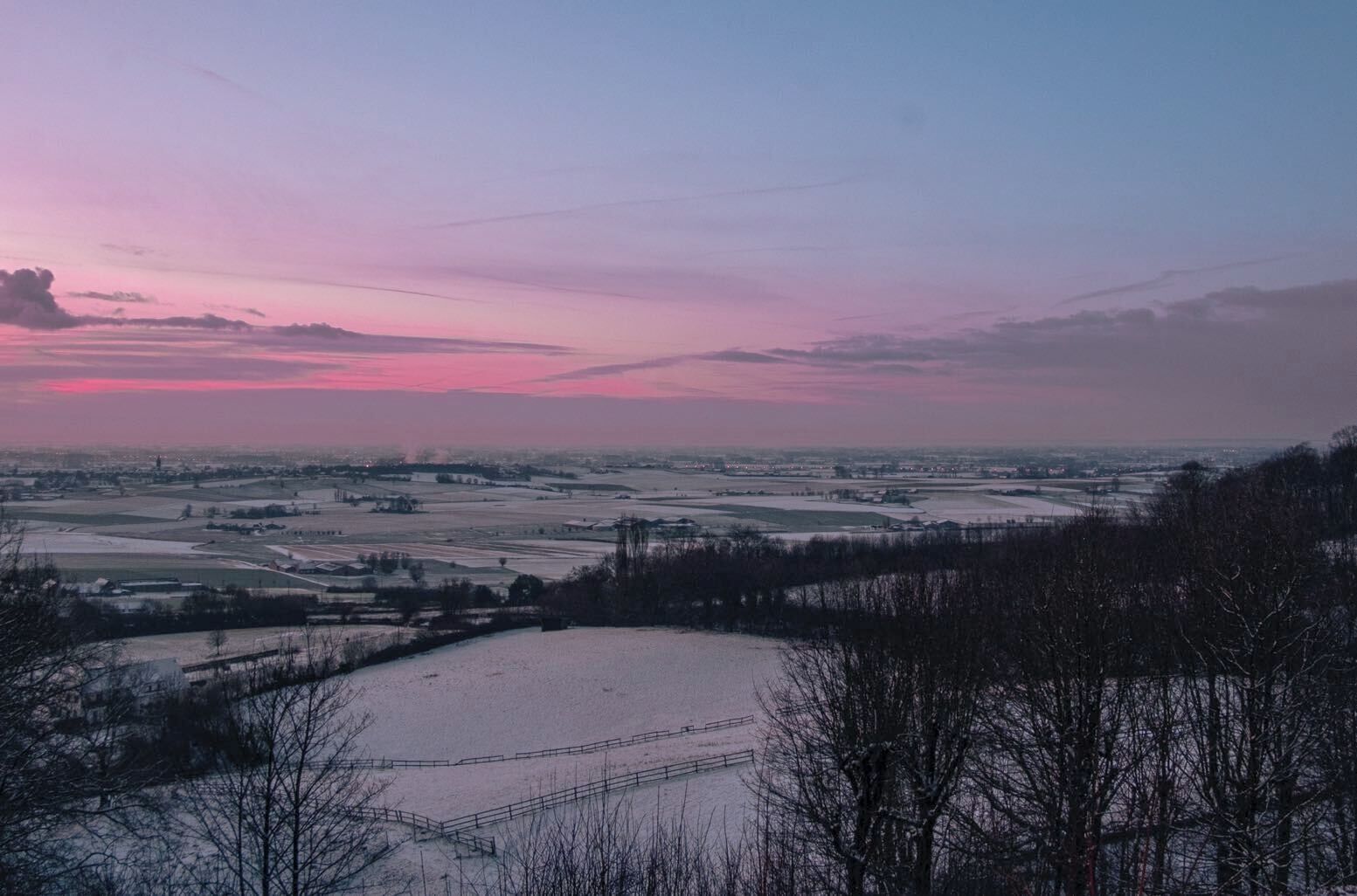 A panoramic view of a winter landscape with snow-covered fields and a distant town.