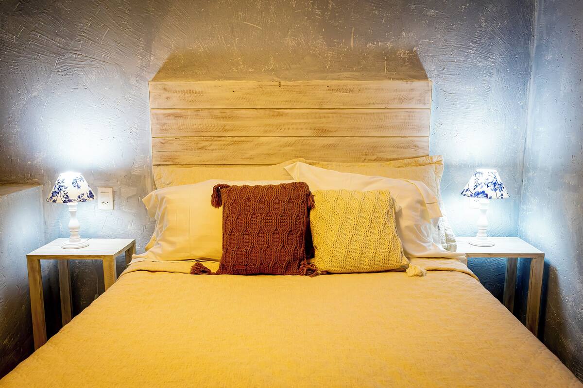 A bed with a wooden headboard, two bedside tables with lamps, and a blanket and pillow on the bed.