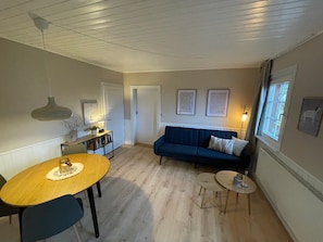 A living room with a wooden dining table, a blue sofa, and a small round table. - Langenberghof Holiday Apartment – Nature Retreat for You and Your Dog (Oberharmersbach)