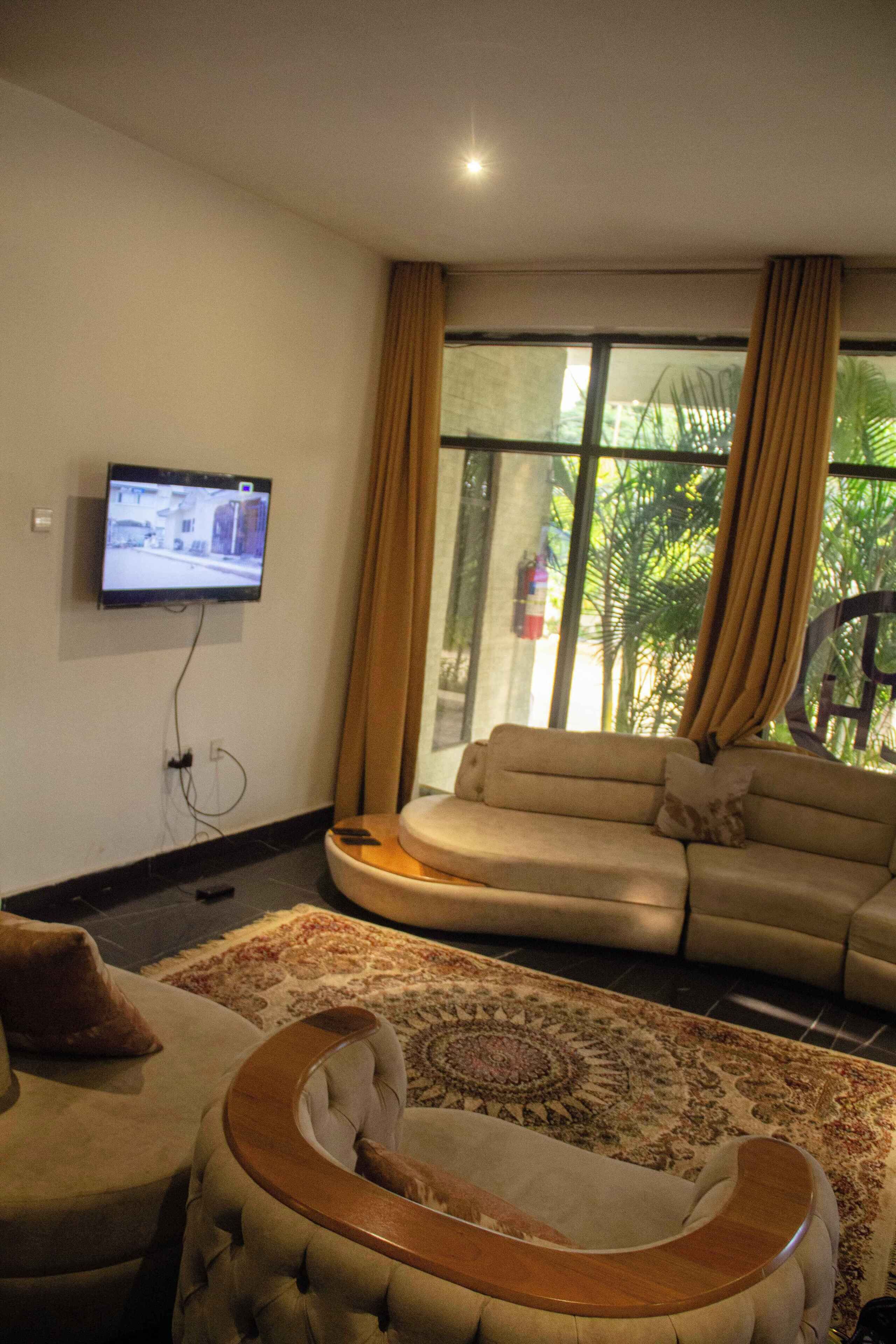Una sala de estar con un sofá, un televisor montado en la pared y un ventanal con cortinas.