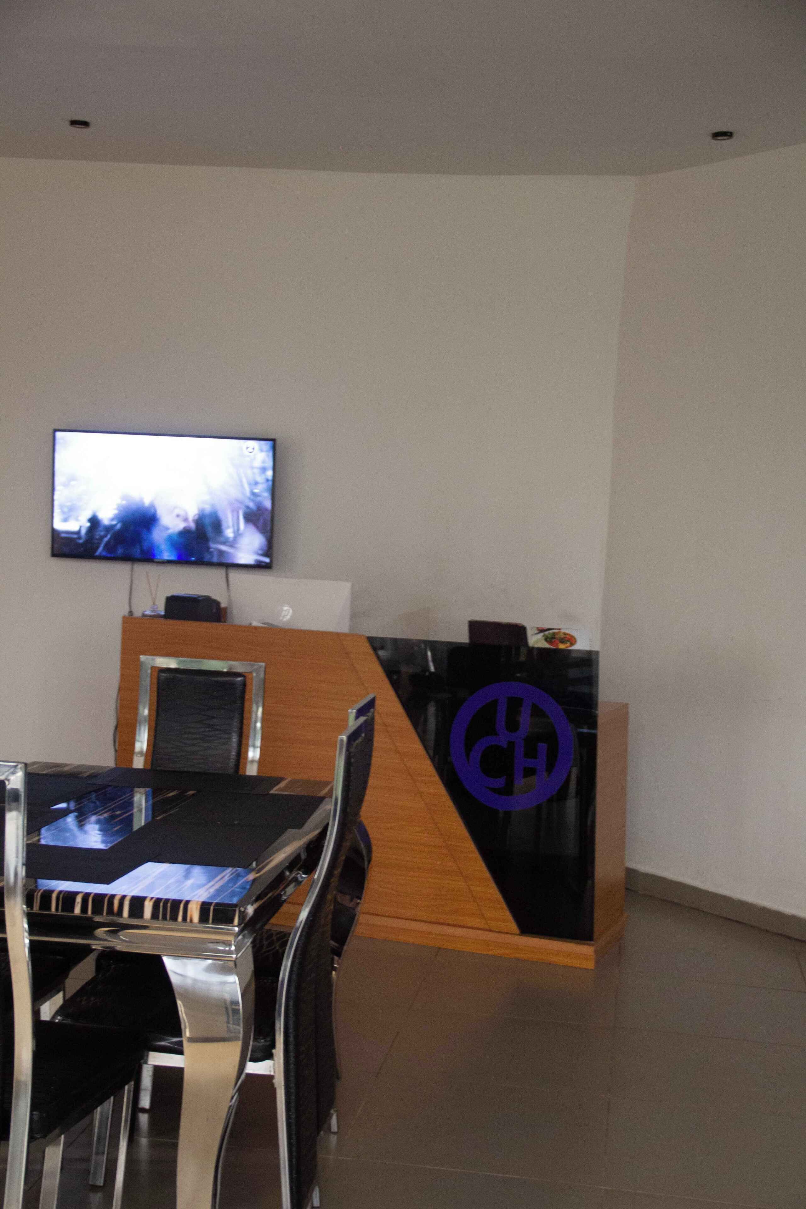 A reception desk with a modern design, a flat-screen TV mounted on the wall, and a dining area with a table and chairs.