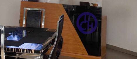 A reception desk with a modern design, a flat-screen TV mounted on the wall, and a dining area with a table and chairs.