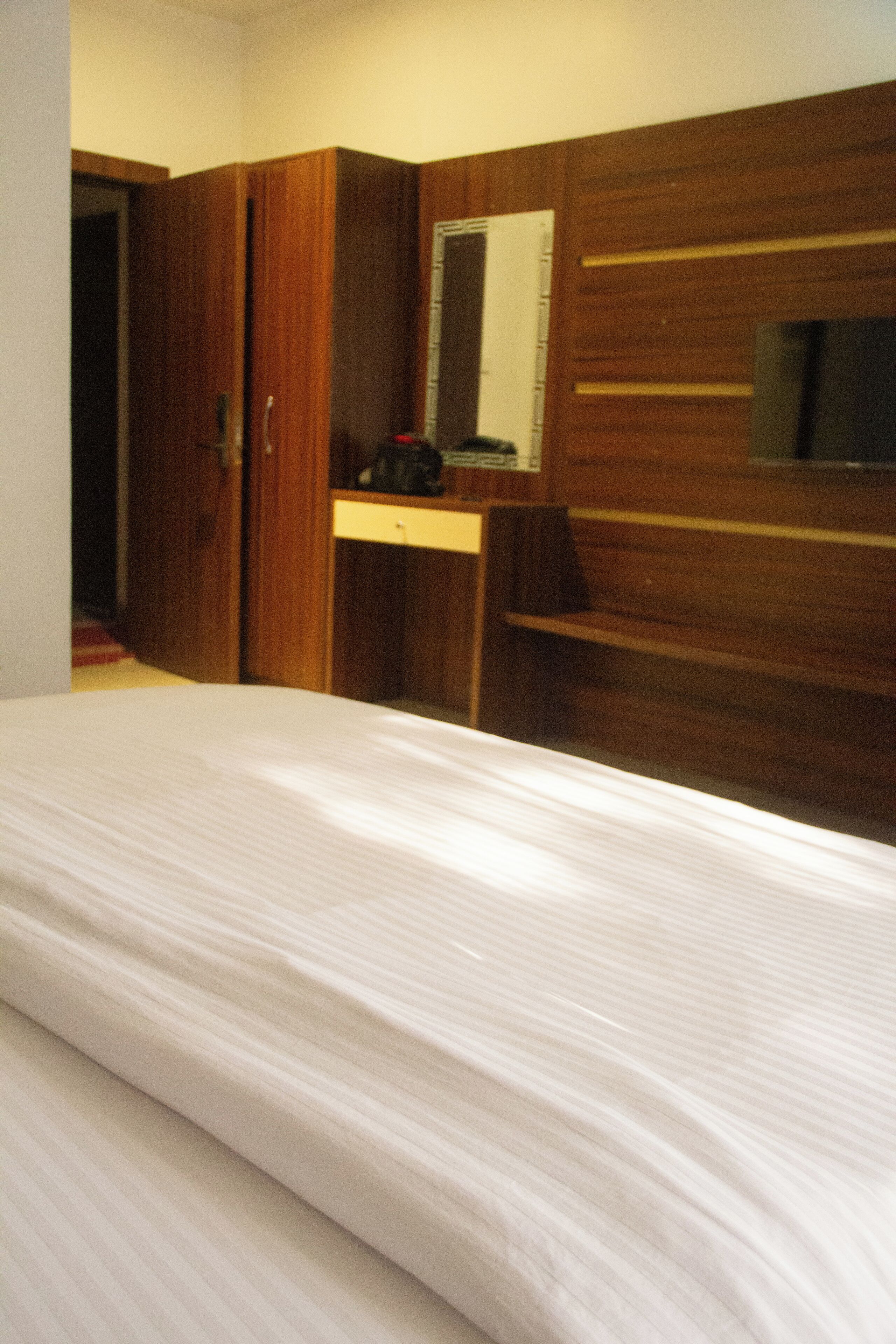 Een hotelkamer met een bed, een houten garderobe en een spiegel.