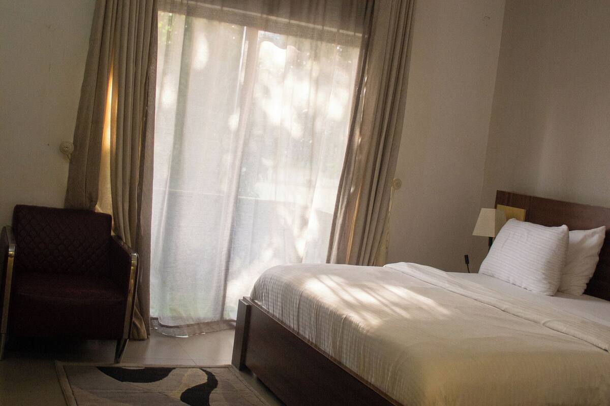 Une chambre d’hôtel avec un lit, une chaise, une fenêtre avec des rideaux et un appareil de climatisation.