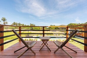 Une terrasse en bois avec deux chaises longues et une petite table, donnant sur une piscine et une végétation luxuriante.