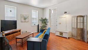 A living room with a sofa, TV, wooden table, and a potted plant. - Charming Soulard Retreat With Historic Character 1 Bedroom Apts (St. Louis)