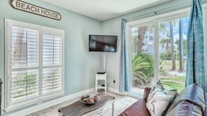 A living room with a television, a coffee table with decorative items, a couch with pillows, and a sign reading "BEACH HOUSE". - Nantucket Cottage 06ab 2 Bedroom Condo (Destin)