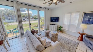 A living room with a sofa, a TV, a plant, a lamp, and a view of the outside.
