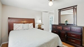 Une chambre à coucher avec un grand lit, une tête de lit en bois, une commode avec des tiroirs, un miroir et un luminaire au plafond.