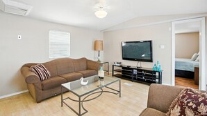 Un salon avec un canapé marron, une table basse en verre, un téléviseur à écran plat et un ventilateur de plafond.