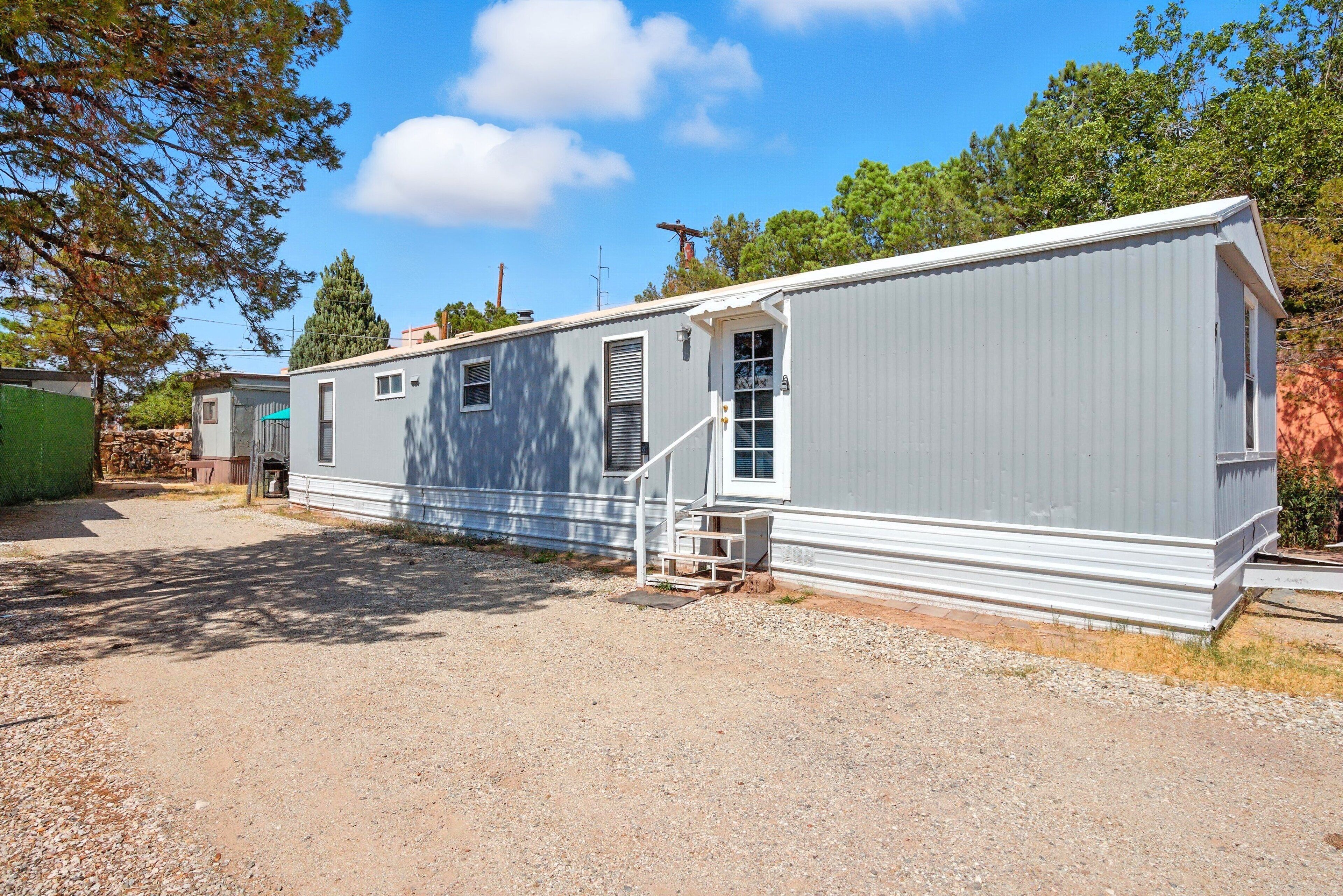 A mobile home with a gravel driveway, a small porch, and a window with a view of the surrounding area.