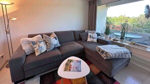 Un saló modern amb un sofà gris, una taula de cafè blanca i un finestral gran que ofereix vistes a l'exterior.