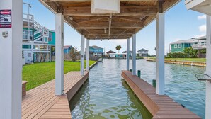 A covered walkway over a canal with wooden decking, white pillars, and a view of houses and greenery. - The Blue Pearl Rp6 4 Bedroom Home (Rockport)