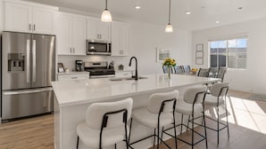 A modern kitchen with white cabinetry, stainless steel appliances, and a central island with bar stools. - Desert Retreat Near Sand Hollow 4 Bedroom Townhouse (Washington)