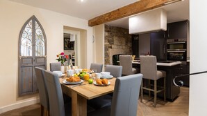 A dining area with a wooden table, grey upholstered chairs, and a breakfast setting including croissants, fruit, and juice. - Stylish 4-bedroom Townhouse in the Heart of Bath (Bath)