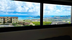 A view from a window overlooking a coastal cityscape with buildings, a clear sky, and the sea. - Stunning Condo With Panoramic Ocean City Views (Cabo San Lucas)