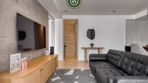 A modern living room with a wooden console, a black leather sofa, a flat-screen TV, and a small wooden table with a plant. - Stylish 1BR Apartment in Roma Norte Near Condesa (Mexico City)