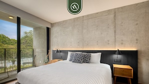 A modern bedroom with a large bed, a concrete accent wall, and a balcony with a view of greenery. - Stylish 1BR Apartment in Roma Norte Near Condesa (Mexico City)